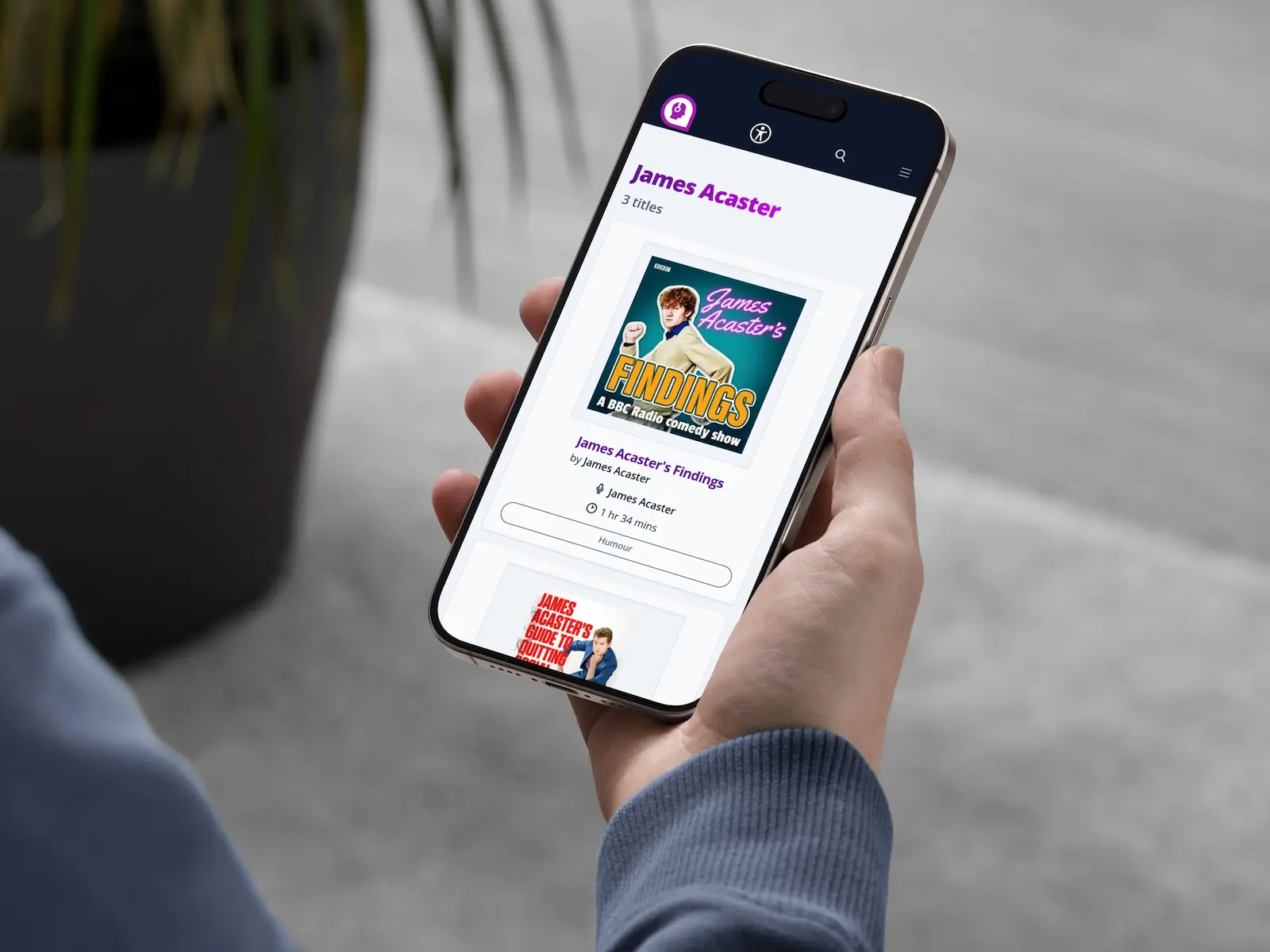 A close-up of a person holding an iPhone open to a list of audiobooks.